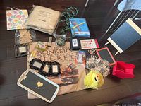 Photo of assorted household items including pillow, easels, frames, comfort kit, and string lights arranged on dark wooden floor.