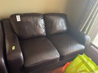 Front view of dark brown leather loveseat showing two seat cushions and cushioned backrest.