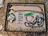 Photo showing assortment of jewelry items including faux pearl necklace, turquoise bracelet, Swarovski marked bracelet with missing stones, and black bead necklaces