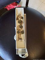 Photo of necklace coiled inside white rectangular padded case with snap closure on black chair.