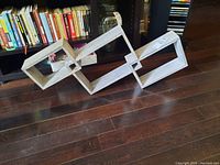Wooden modern style wall shelving unit with three diamond-shaped compartments displayed flat on hardwood floor near bookshelf.