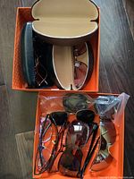 Top-down view of a box containing several pairs of glasses and sunglasses, some in cases and some loose, showing various frame styles and colors.