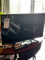 Photo of RCA LED TV with black frame and remote control visible on a table reflecting window light.