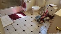 Bathroom setting showing burgundy shower curtain, bath mat, towels, white trash bin, hamper, faux flowers, wall clock, and metal fan-shaped trash basket on tiled floor