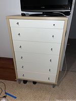 Front view of the five-drawer chest with light wood frame and white drawer fronts, showing five drawers with round metal knobs and a TV on top.
