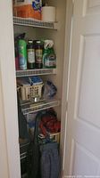 Shelving closet with cleaning products including spray bottles, boxed items, and vacuum cleaner accessories.