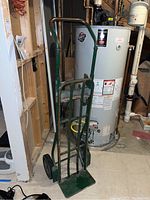Full view of green metal hand truck next to water heater in basement, showing overall condition and frame.