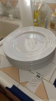 Stack of six white Le Creuset dinner plates on a kitchen counter.