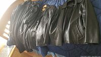 Four men's jackets displayed on a bed, all in black or dark colors including hooded and leather styles.