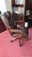Front side view of brown leather office chair with visible nail head accents on armrests.