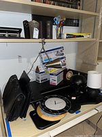 Shelves with various office accessories including clocks, lamps, toner cartridges, scissors, and portfolios