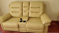 Front view of cream leather reclining loveseat with center console and remote control placed in cup holder.