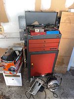 Full view of the red and black Test Rite tool chest on wheels with drawers and cabinet, power tools on floor, Black & Decker box nearby.