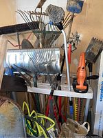 Photo showing yard tools including metal leaf rakes, shovels, Black & Decker electric hedger, pruning loppers, broom, and tools rack.