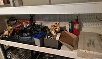 Shelving unit with various tools, electric cords, and boxed items including fire extinguishers in background