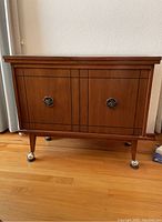 Front view of vintage wooden credenza with two doors and ornate handles on castor wheels.