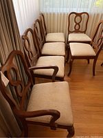 Full side view of six wooden dining chairs showing carved backs, upholstery, and front legs
