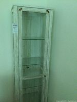 Full view of tall narrow whitewashed display cabinet showing front glass door and interior shelves