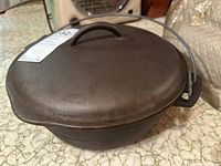 Cast-iron Dutch oven with lid, viewed from above showing lid and handle. Dark brown color and rough texture of cast iron.