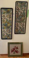 Pair of two rectangular framed embroidered wall hangings with floral patterns hanging vertically on a wall.