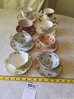 Overview of seven cups and saucers on table showing variety of floral china designs and gold trim.