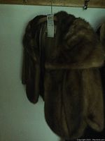 Full view of the brown fur cape hanging on a hanger showing the luxurious fur texture and shape.
