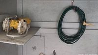 Self-propelled sprinkler on metal rack shelf with green garden hose hanging next to it.