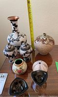 Front view of six ceramic and glass accent pieces arranged on a table with measuring tape for scale
