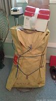 Overview of yellow canvas storage bag containing folded Zodiac Type 1505 inflatable dinghy, with Gamefisher trolling motor head and red-white battery box on top