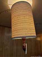 Photo showing the hanging lamp illuminated with woven fabric shade and wooden finial, highlighting the textured pattern of the shade.