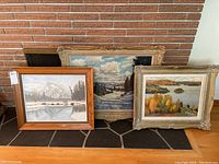 Three framed oil paintings displayed against brick fireplace