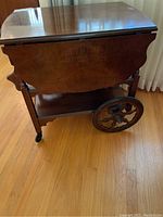 Full side view of the antique wooden serving cart showing large decorative wooden wheels and drop-leaf side panel.