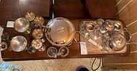 Overview of silver plated tea set with brass stemware and additional serving pieces on wooden table.