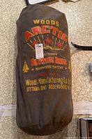 Rolled brown canvas stuff sack with printed Woods Arctic Underdown Sleeping Robe logo