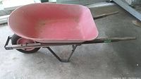 Full side view of the red metal wheelbarrow with wooden handles on the floor.