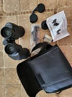 Black Optic Vision binoculars with neck strap, lens covers, instruction manual, and carrying case laid out on a tiled surface.