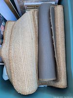 Photo of rolled floor mats including beige woven mats and a gray fabric mat