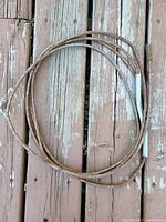 Single image showing a metal drain snake coiled on a wooden surface, heavily rusted