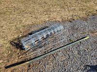 Overall view of field fence roll and green T-post lying on ground showing approximate length and condition.