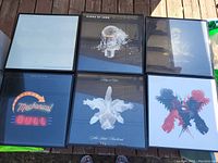 Six framed Kings Of Leon album covers laid out on wooden deck, showing various album art styles and colors.