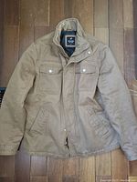 Brown Denver Hayes utility jacket with front flap pockets and zipper closure laid flat on floor.