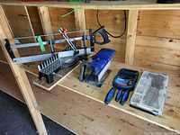 Hand miter saw with adjustable angle guide and clamp, T-handle hex key, blue express wrench, rivet tool, and small file set in plastic case on wooden shelf.