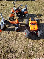 Three outdoor ride-on toys on grass including the battery-powered motorcycle, pedal tricycle, and large monster truck