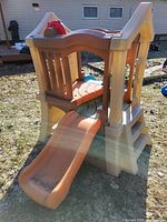 Side view of the playstructure showing orange slide, tan frame, and small climbing stairs on the rear.