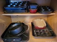 Front view of upper shelf with multiple baking pans and muffin tins stacked together. Lower shelf holds metal roasting pan, stacked round cake pans, plus a pan rack on a rectangular baking pan.