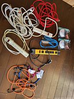 Power strips and multiple extension cords in various colors and lengths arranged on floor.