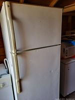 Exterior view of the white refrigerator with top freezer and bottom fridge doors showing door handles and minor dents.