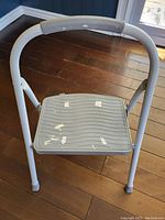 Top-down view of gray step stool showing peeling white paint on plastic step platform, metal frame handle, and rubber feet caps on hardwood floor.