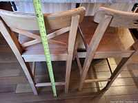 Three wooden bar stools placed side by side, showing approximate height with a measuring tape around 29 inches tall.