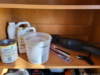 Wooden shelves holding wood finish bottles, measuring containers, and a small black hand vacuum.